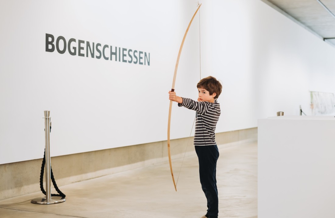 Ein Junge steht mit einem Bogen in der Hand in einem Gang des Museums. Foto: Katja Velmans © LVR-LandesMuseum Bonn 