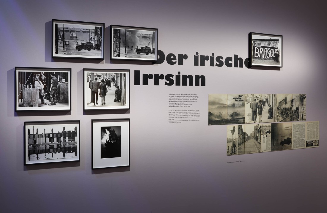 Schwarz-weiß-Fotos hängen an einer fliederfarbenen Wand in der Ausstellung.