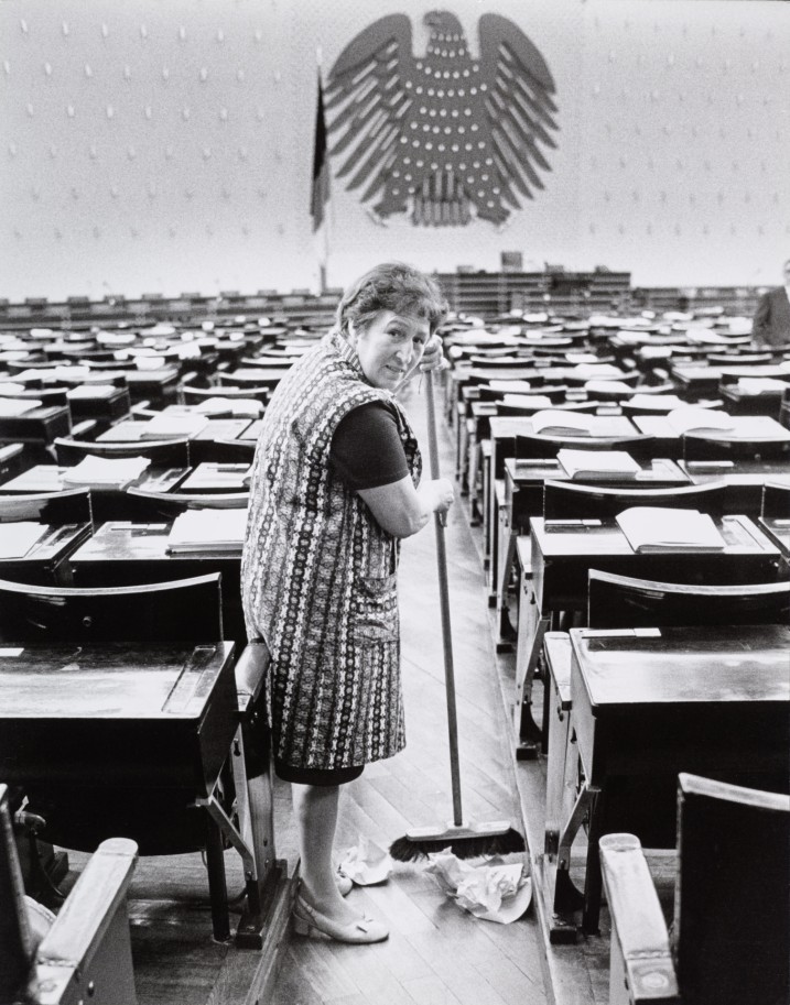 Eine Putzfrau fegt im Deutschen Bundestag und schaut in die Kamera.