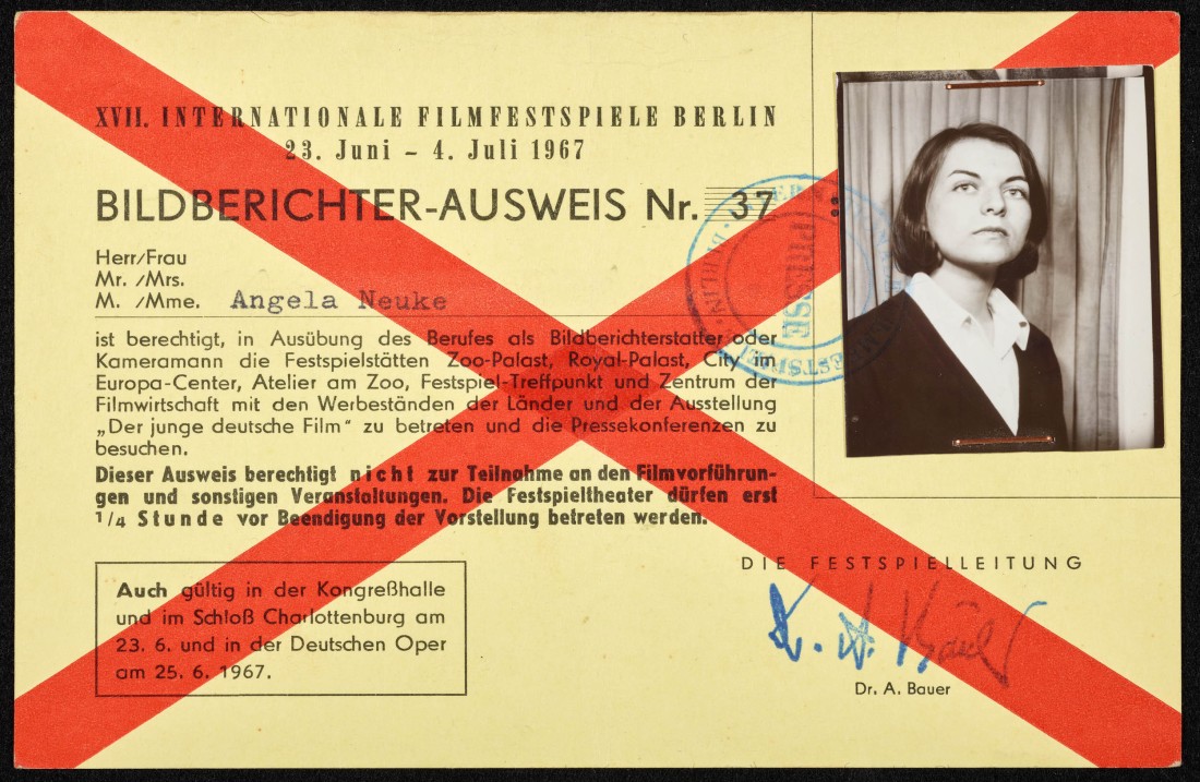 Ein gelblicher Ausweis mit einem roten, x-förmigen Kreuz über die gesamte Größe und einem Foto von Angela Neuke. 