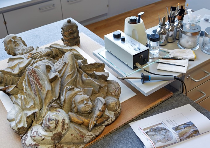 Eine Holzskulptur eines Heiligen liegt auf dem Arbeitsplatz, daneben Geräte. Foto: J. Vogel, LVR-LandesMuseum Bonn.