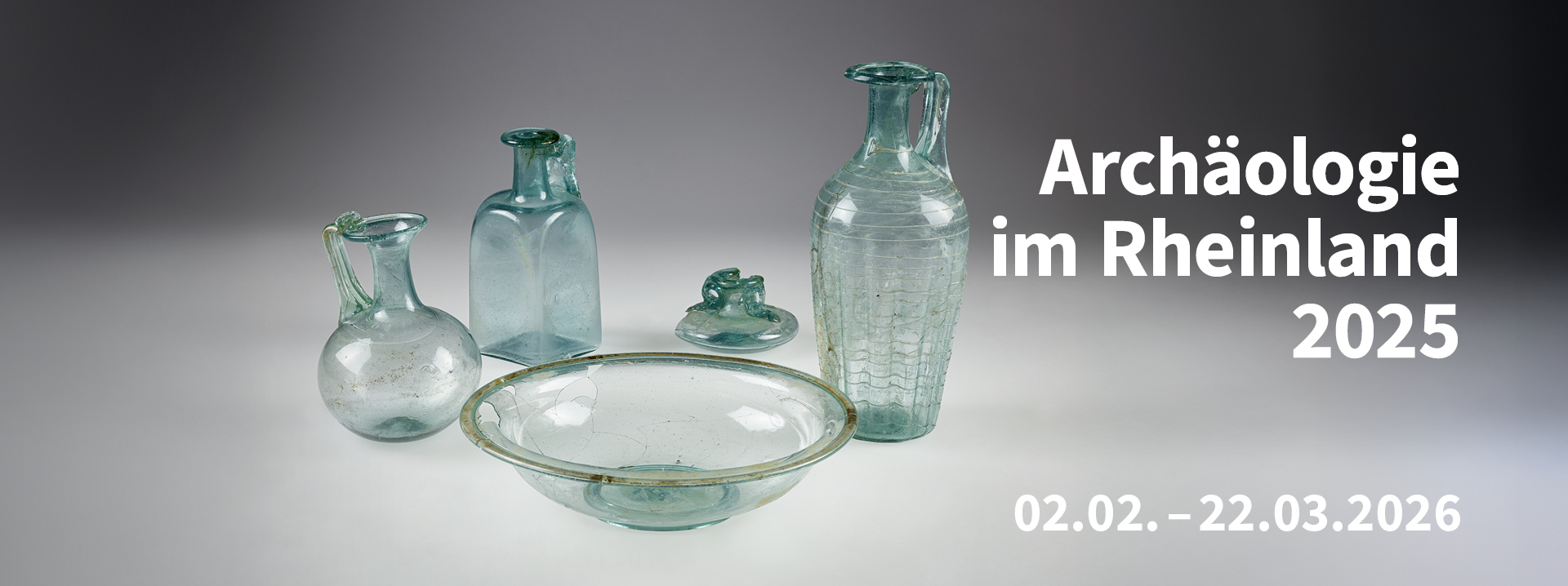 Verschiedene archäologische Glasgefäße stehen vor einem grauen Hintergrund. 