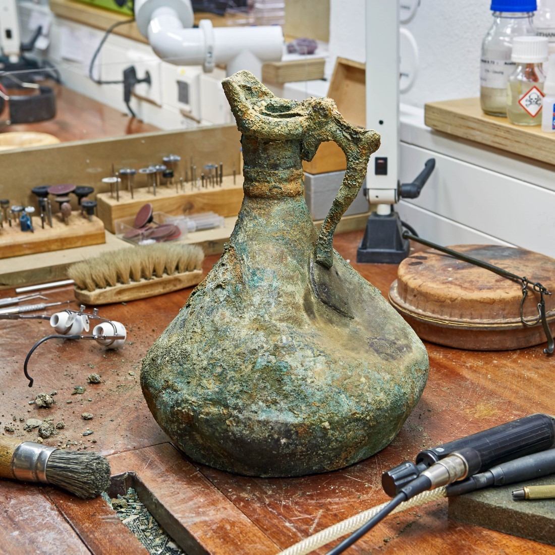 Eine Kanne wird auf dem Arbeitstisch in der Restaurierungswerkstatt vorsichtig bearbeitet. Foto: J. Vogel, LVR-LandesMuseum Bonn.