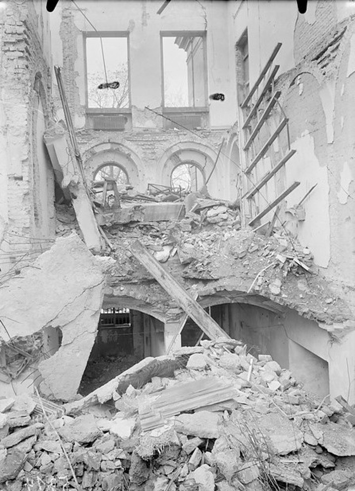 Schwarz-weiß Fotografie eines zerstörten Gebäudeteils. Drei Wände stehen, der Rest ist zusammen gebrochen.