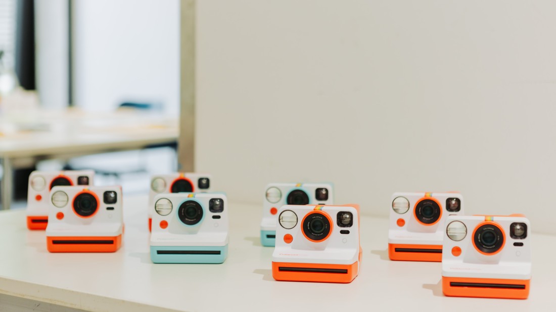 Viele farbenfrohe Polaroid-Kameras sind auf einem Tisch platziert. 