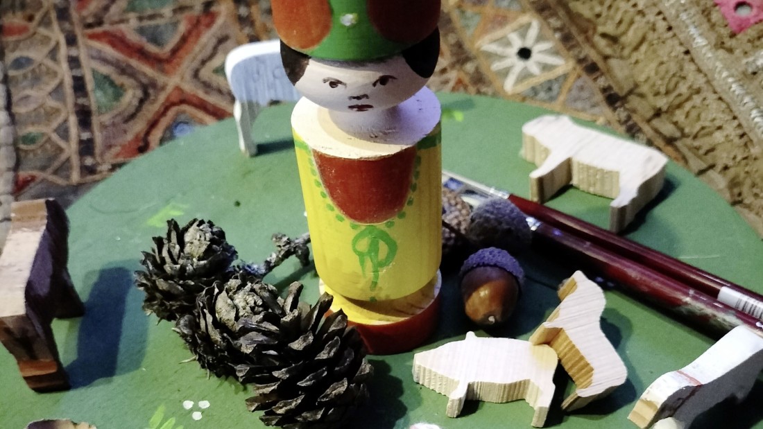 Eine bemalte Holzfigur aus dem Erzgebirge ist neben Tannzenzapfen, Pinselns und weiteren Holzarbeiten platziert.