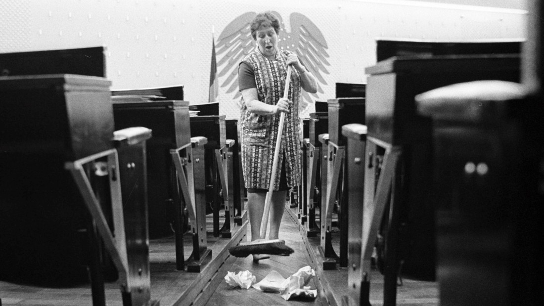 Eine Raumpflegerin säubert den Deutschen Bundestag und schaut in die Kamera.