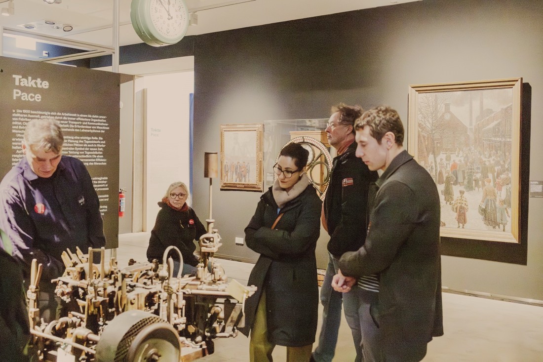 Eine Gruppe steht vor einem Objekt in der Ausstellung "Sch&ouml;ne neue Arbeitswelt. Traum und Trauma der Moderne".