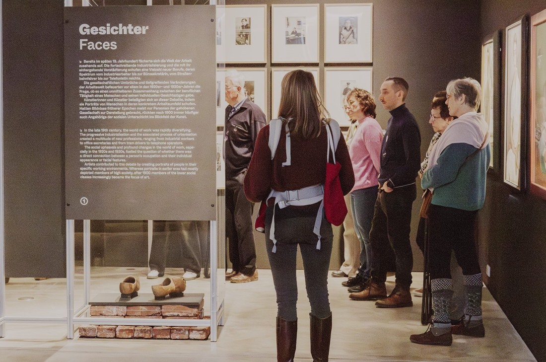 Ein Gruppe steht vor Fotografien in der Ausstellung "Sch&ouml;ne neue Arbeitswelt. Traum und Trauma der Moderne".