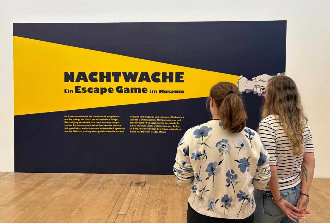 Zwei Besucherinnen betrachten das Keyvisual zum Escape Game Nachtwache im Museum.