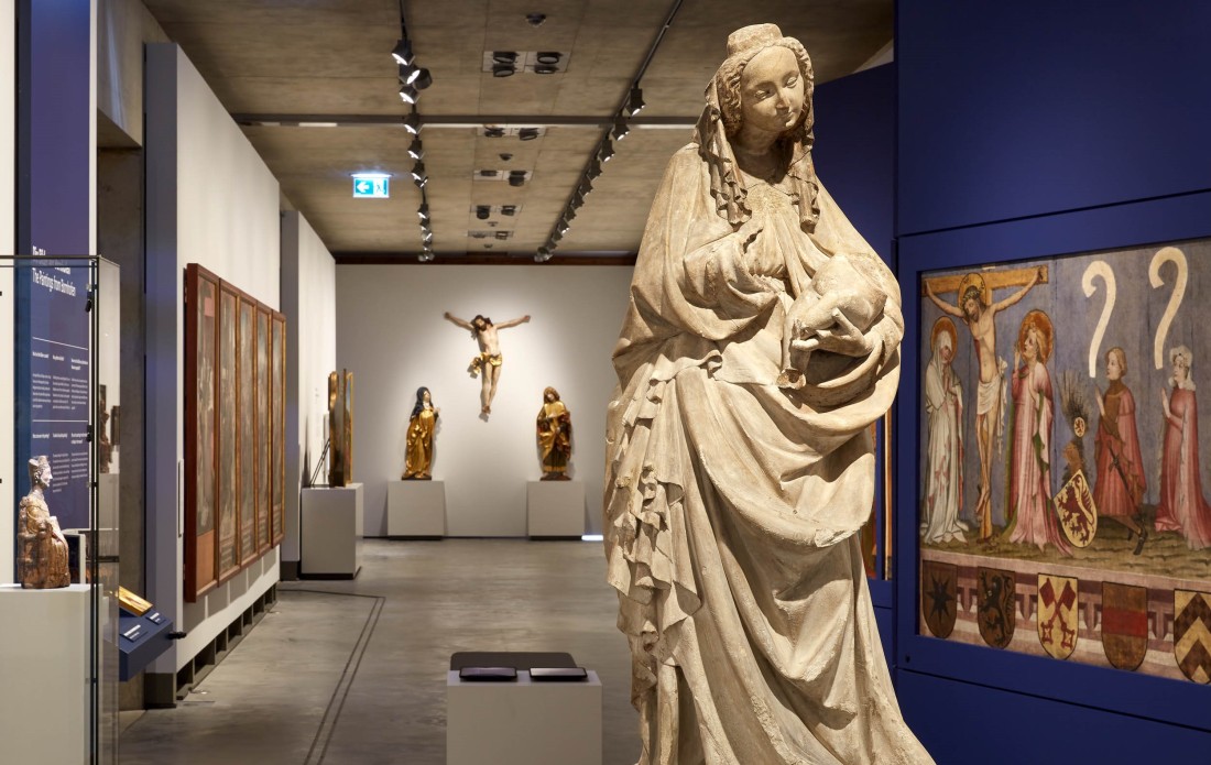 Im Vordergrund eine gotische Madonna mit Kind, im Hintergrund weitere Altarretabel und christliche Figuren.