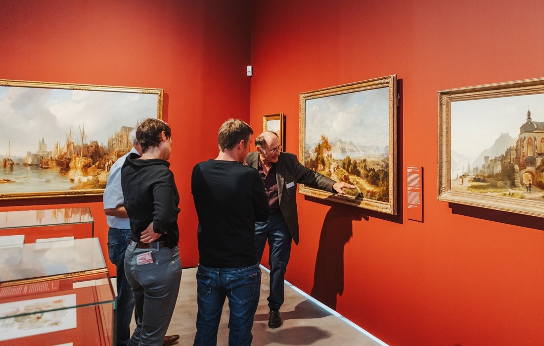 Eine Gruppe steht vor Gem&auml;lden der Rheinromantik.