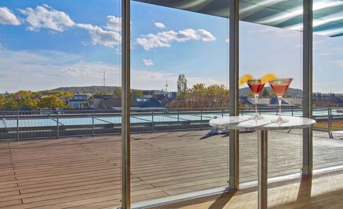Dachterrasse des LVR-Landesmuseums Bonn mit Ausblick in die Landschaft und einem Tisch mit zwei Getr&auml;nken im Vordergrund.