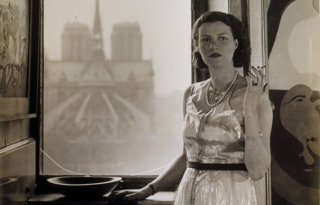 Plakatmotiv zur Ausstellung "Fluchtpunkt Paris" mit Peggy Guggenheim am Fenster ihres Pariser Appartements, im Hintergrund Notre Dame. 