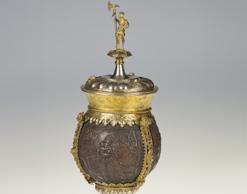Den Mittelpunkt des reich verzierten Pokals bildet eine geschnitzte Kokosnuss. Sie liegt auf dem vergoldeten Fuß des Pokals und trägt einen Deckel mit einer kleinen Figur mit einer Hellebarde.