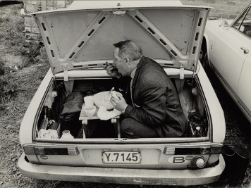Ein Mann sitzt im geöffneten Kofferraum eines Autos und isst aus einer Schüssel.