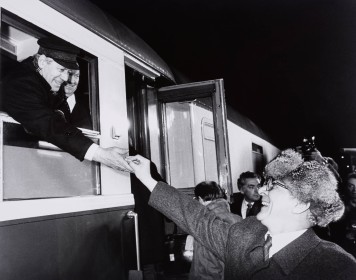 Ein schwarz-weiß Foto von Erich Honecker, der Helmut Schmidt ein Hustenbonbon aus einem Zugfenster reicht.