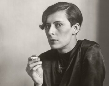 Die Schwarz-weiß Fotografie zeigt eine Frau mit modernem Kurzhaarschnitt, die eine Zigarette raucht.