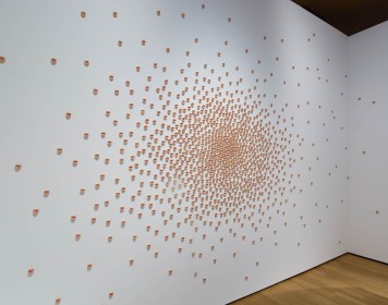 Die Installation besteht aus 1000 Kussmündern oder Anussen, die an einer weißen Wand kleben.